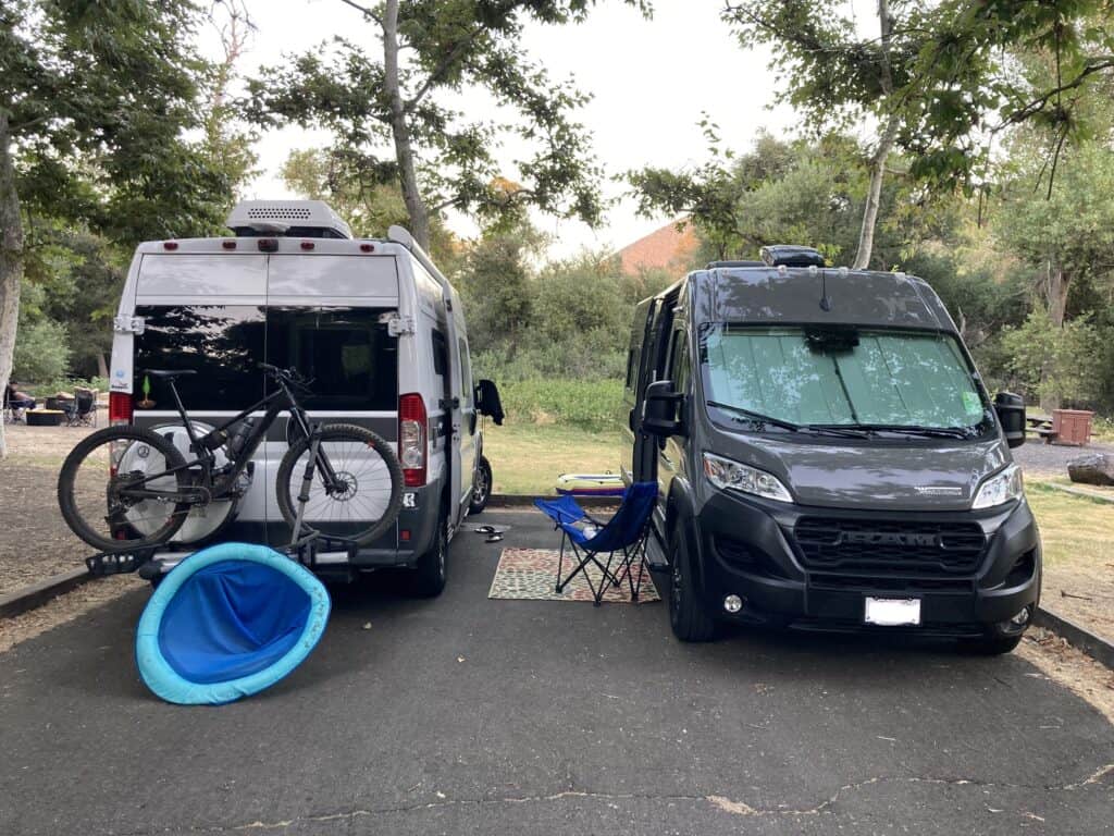 two vans parked next to each other on the clear lake campsite parking pad.