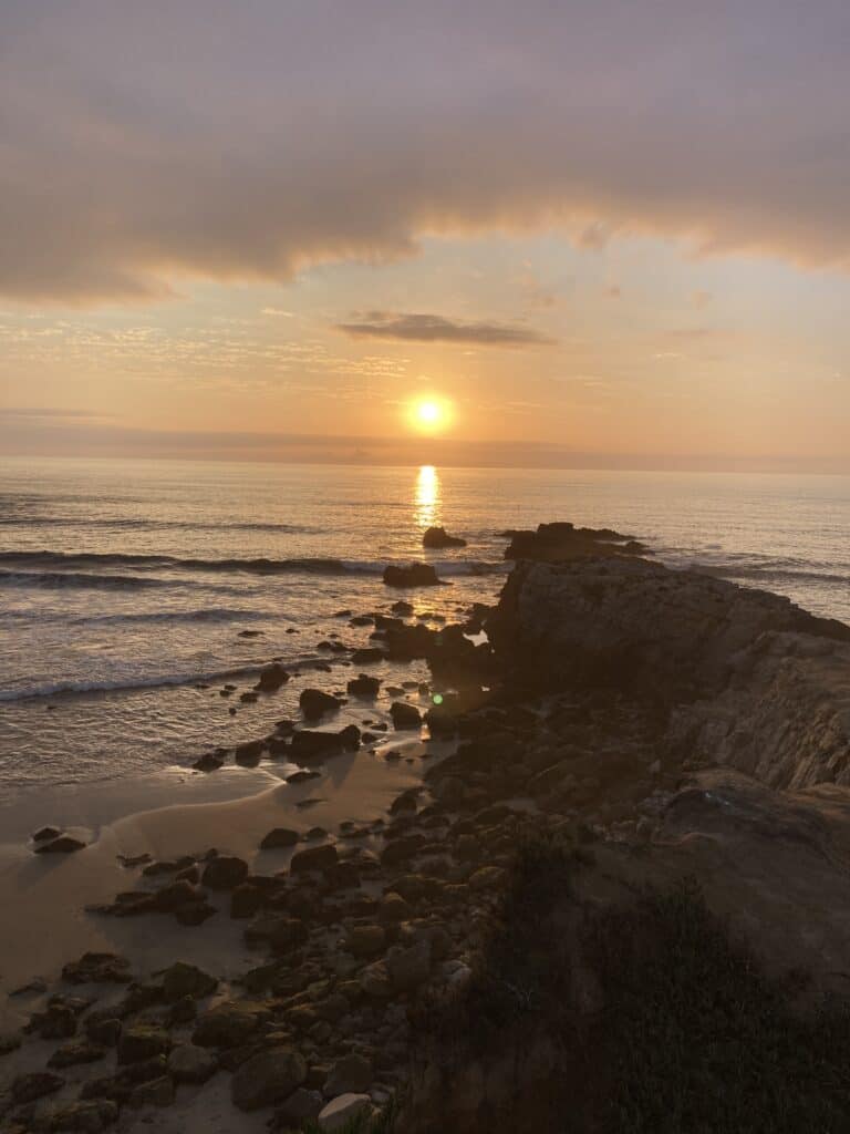 A beautiful orange sunset looking out over rocks and the ocean.