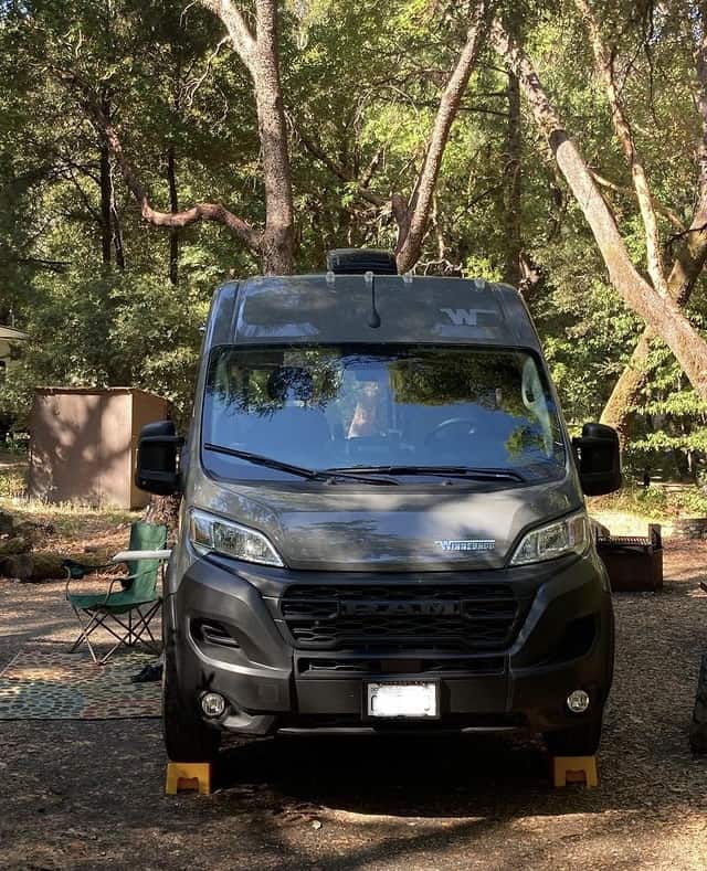 looking headon at our van parked in our campsite with green trees and a camping chair.