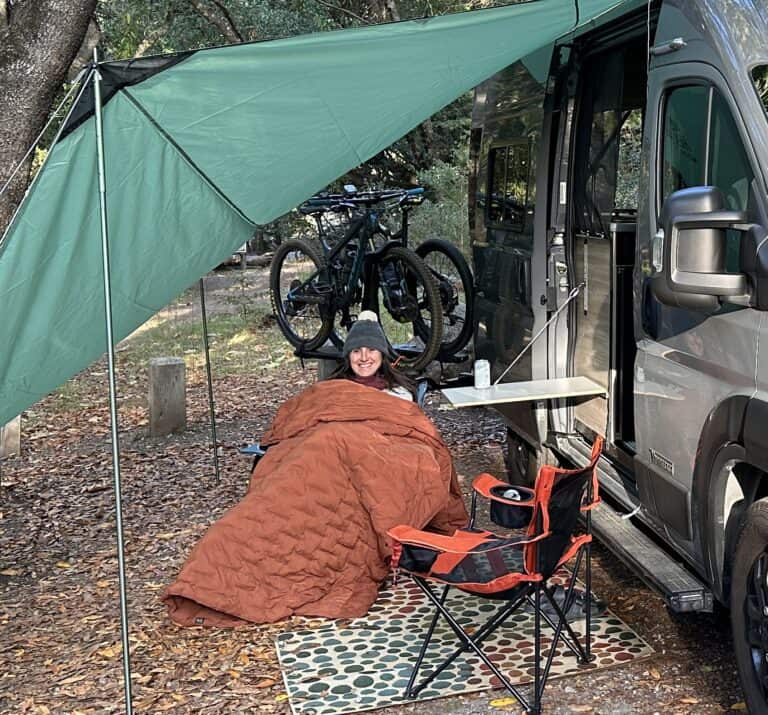 woman with a down quilt over her as she sits under a canopy