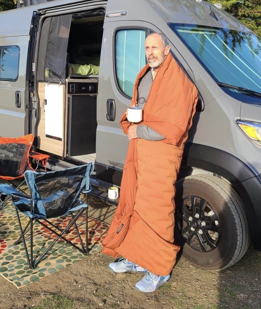 man standing next to a van wearing a down quilt