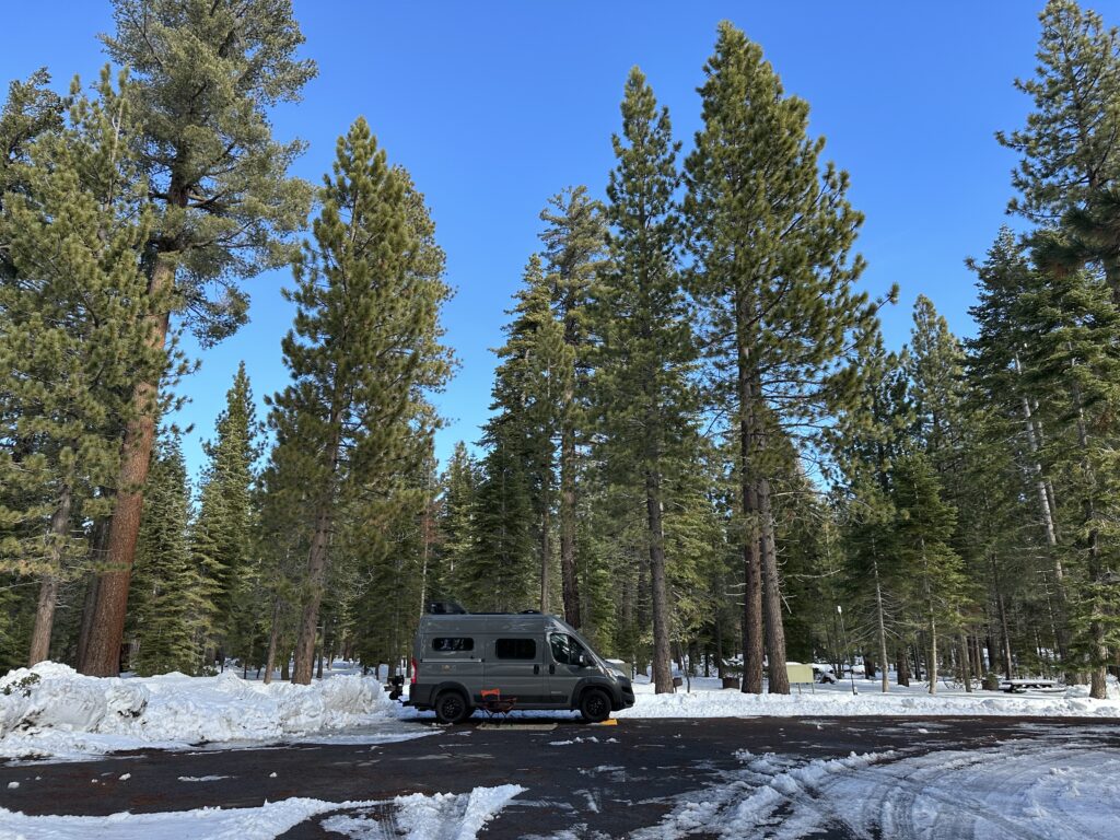 a gray van in the distance with snow and tall pine trees in the background