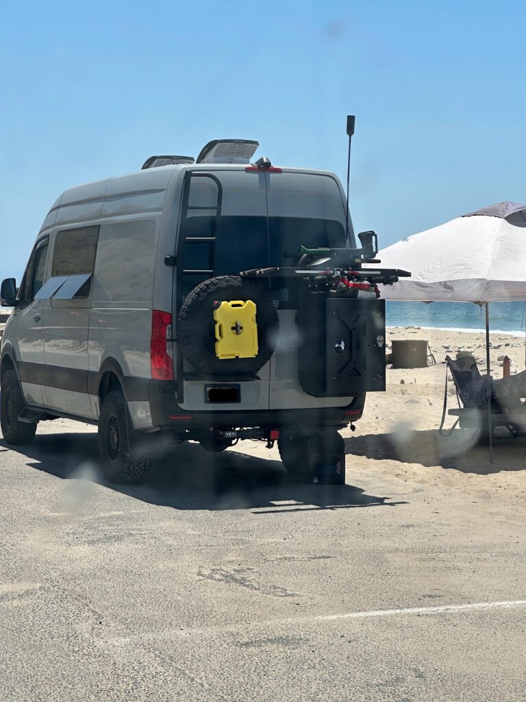 sprinter van parked on pavement alongside their beachfront campsite