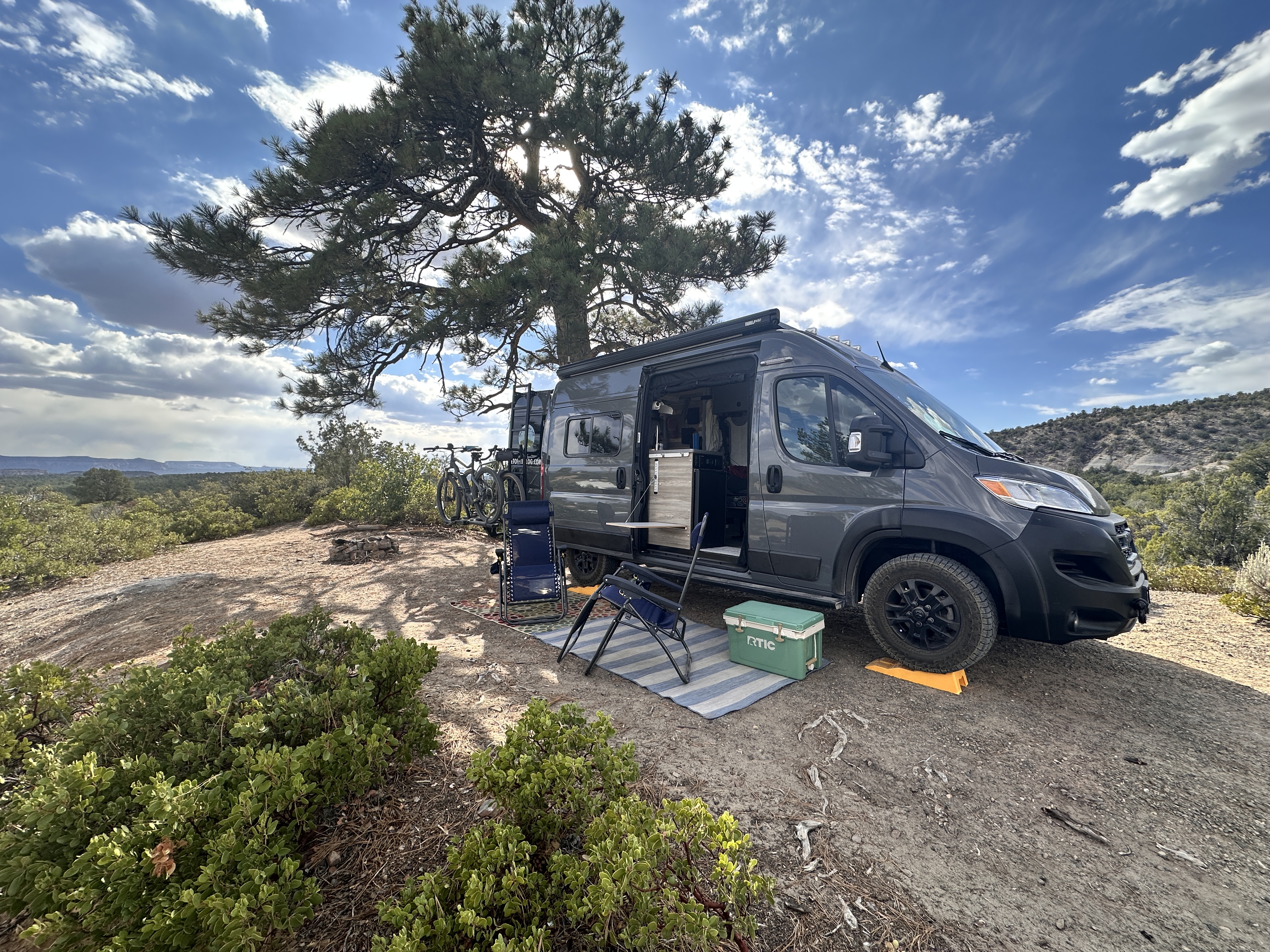 van on a hill with blue sky and a big tree in the distance